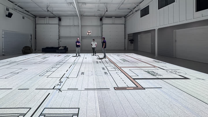 Looking down the length of a floor plan projected at 1:1, with three people standing in the great room at the far end.