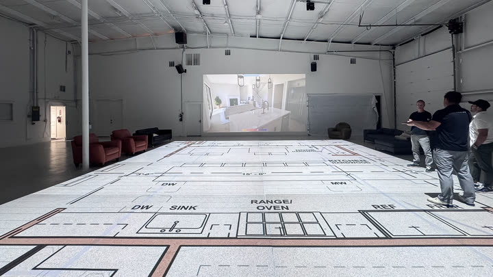 A kitchen plan projected on the studio floor — dishwasher, sink, range and refrigerator marked at true size — with a rendering of the same kitchen on the wall behind it.