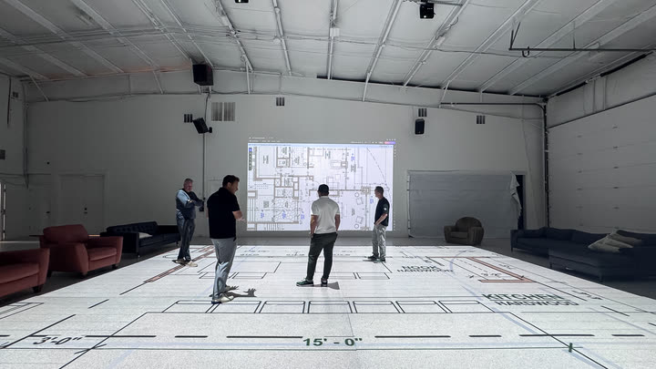 Five people standing on a projected kitchen plan, talking through it, with the full drawing displayed on the wall behind them.