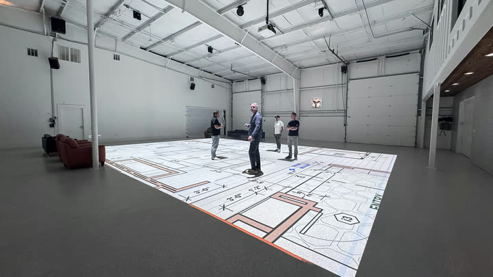 The walkthrough space, with a floor plan projected across the floor and people standing inside it.